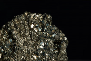 Primer plano de un mineral brillante con cristales metálicos dorados sobre un fondo negro.