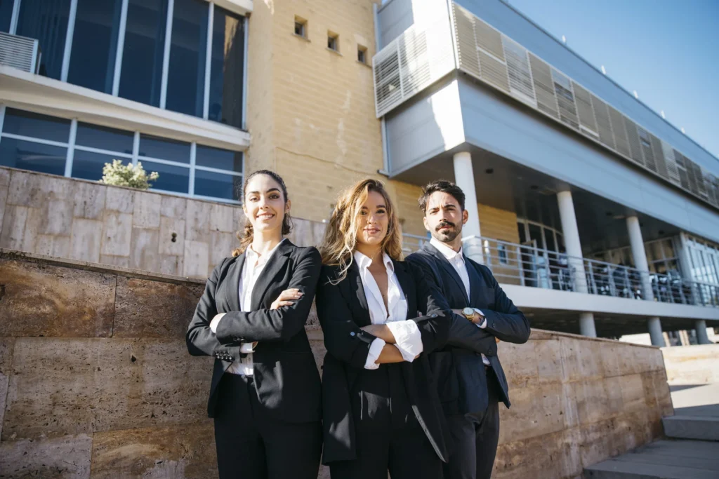 Equipo de profesionales vestidos con traje posando con los brazos cruzados frente a un edificio corporativo moderno.