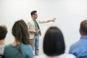 Hombre realizando una presentación en público ante una audiencia en una sala de formación o conferencia