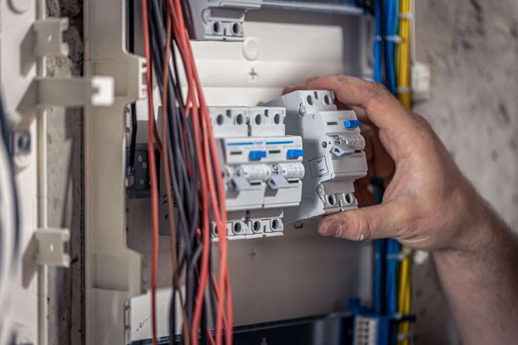 Electricista instalando o ajustando un interruptor automático en un cuadro eléctrico con cableado visible.