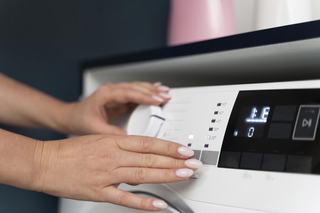 Manos ajustando el selector de programa en una lavadora moderna con panel digital y controles táctiles.